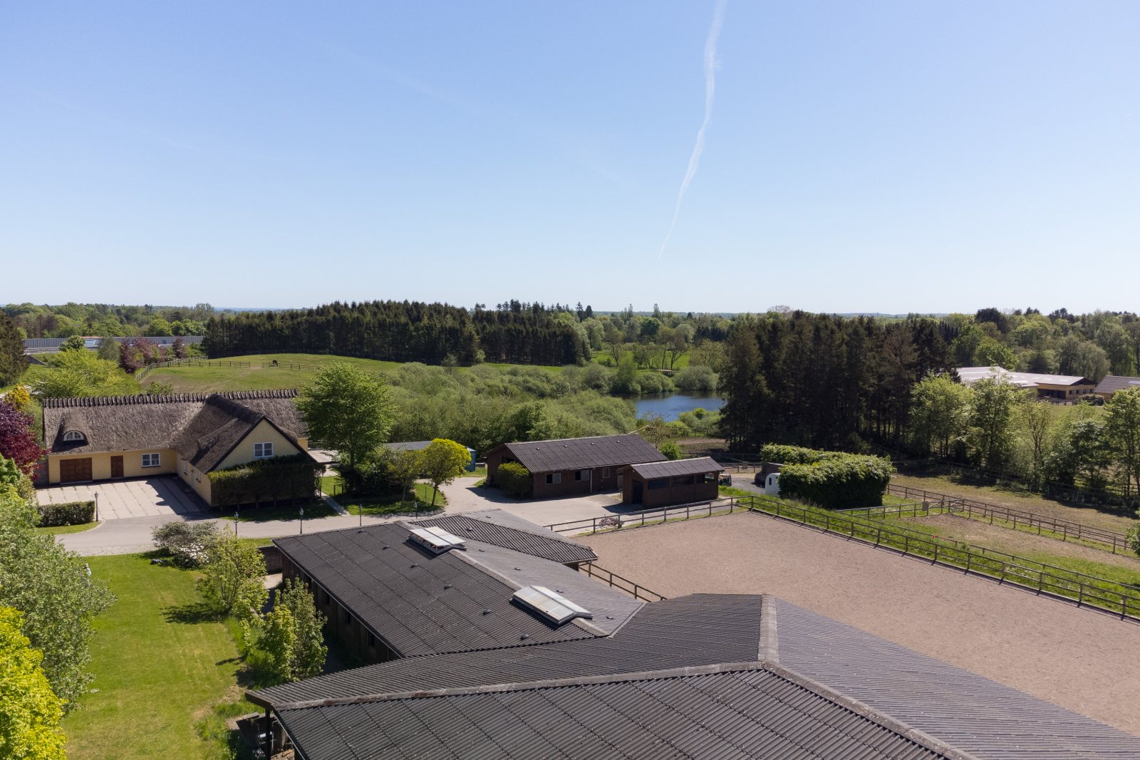 Luftfoto af Sandbjergvej med stråtækt hus, ridebane og grønne omgivelser